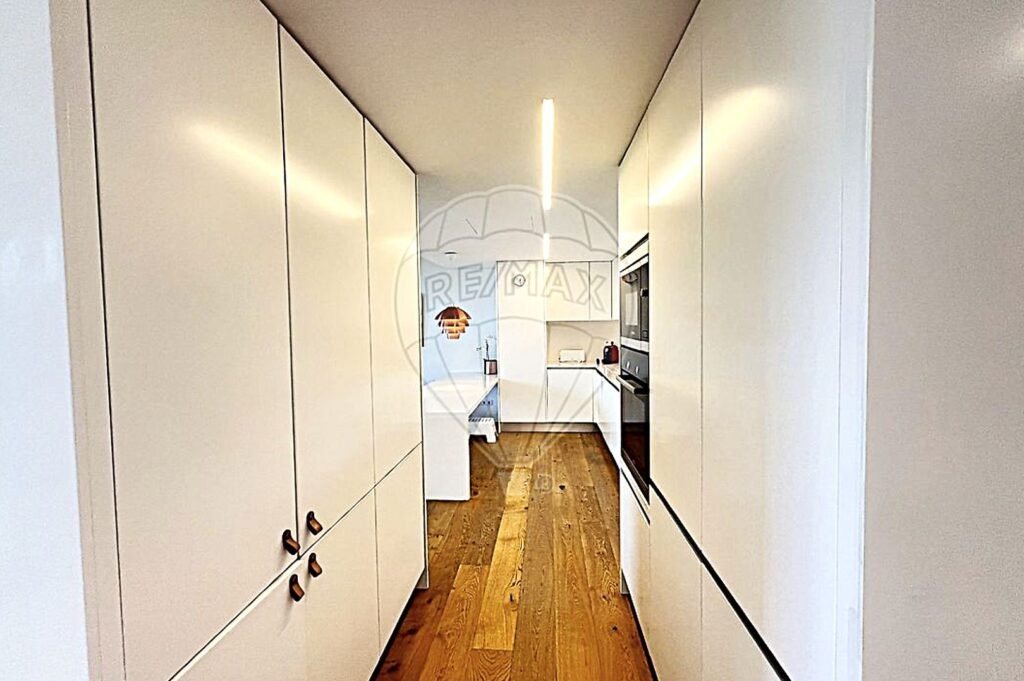 Bright kitchen corridor lined with floor-to-ceiling white storage cupboards.