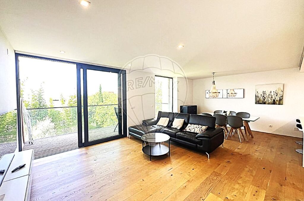 Sunlit lounge area with floor-to-ceiling windows looking out onto lush green garden plants.